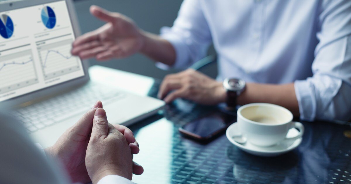Two people are sitting at a desk and going over a deal. Next to them is a laptop with pie charts on it.