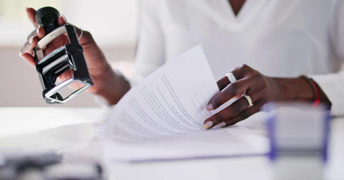 A woman holding a piece of paper in one hand. In her other hand, she holds an official notary stamp.