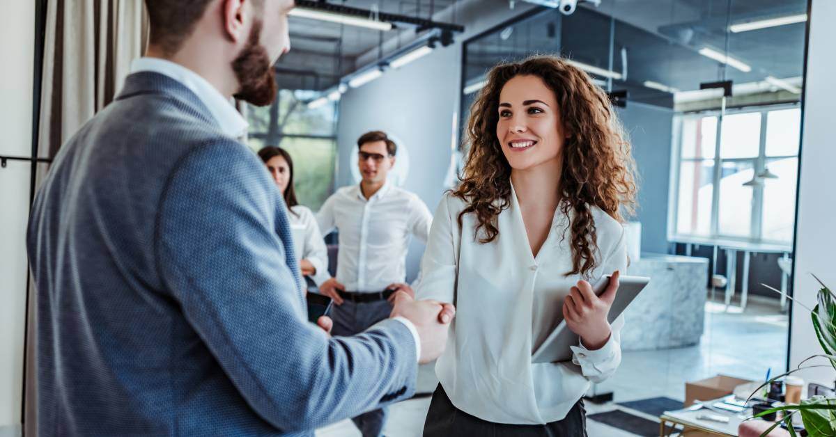 Two professionals are standing in an office. The man and woman are shaking hands after reaching a collaborative agreement.