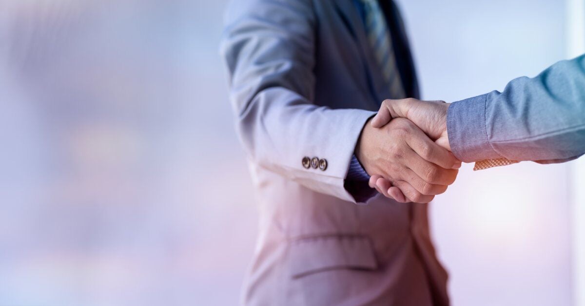 Two people in suits are reaching out to shake hands and make a deal. The background is blurry to focus on the handshake.