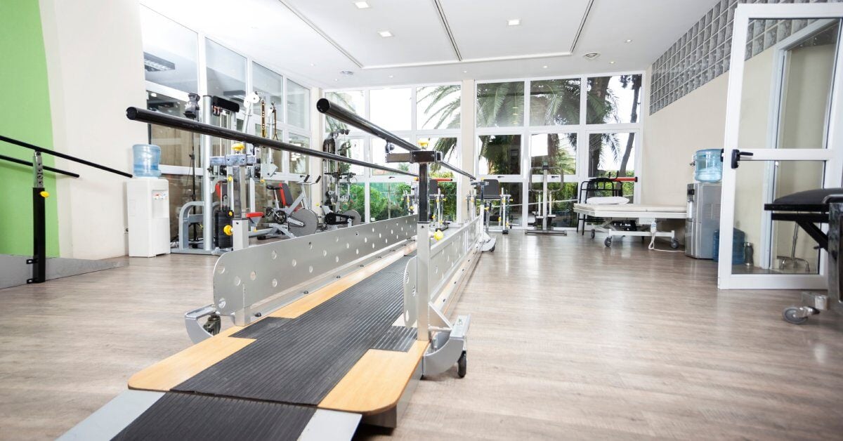 The interior of a physical therapy clinic. A small ramp and path with guard rails for walking therapy sits in the center.